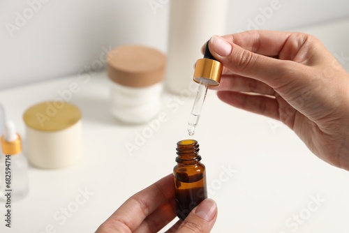 Woman with bottle of cosmetic serum and pipette at white table, closeup