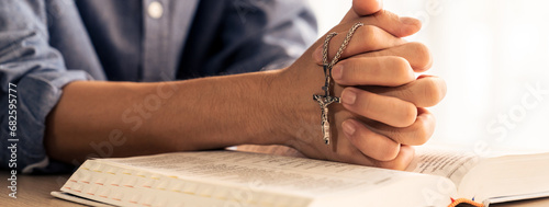 Asian male folded hand prayed on holy bible book while holding up a pendant crucifix. Spiritual, religion, faith, worship, christian and blessing of god concept. Blurring background. Burgeoning.