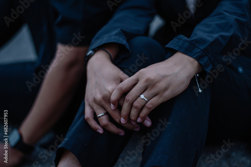 The couple held hands in a very romantic way, the woman's hand was wearing a wedding ring and white clothes while the man was wearing black clothes photo
