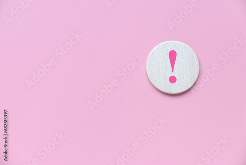Wooden circle with exclamation mark over a pink background. photo