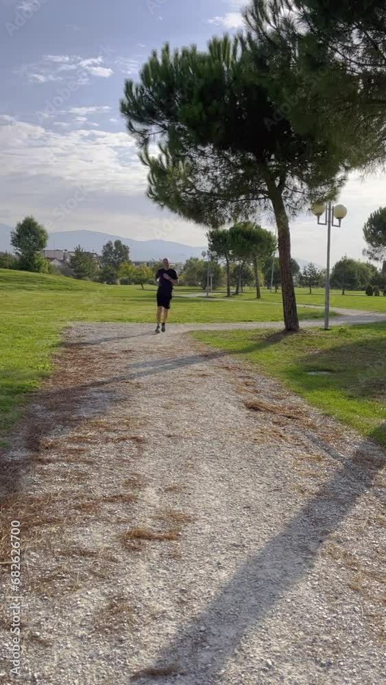 Man jogging on pathway amidst trees. Male athlete exercising in park against sky during summer. He is in sportswear. Man jogging on pathway amidst trees. Male athlete exercising in park against sky during summer. He is in sportswear.