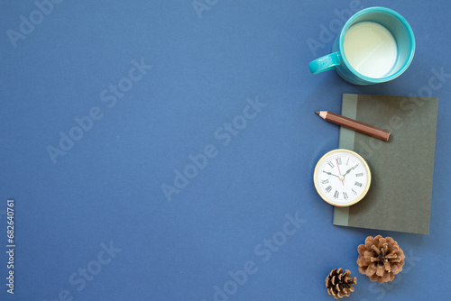 Notebook, clock, colored pencil, cup of milk with pine cone on navy blue background. top view, copy space. workspace
