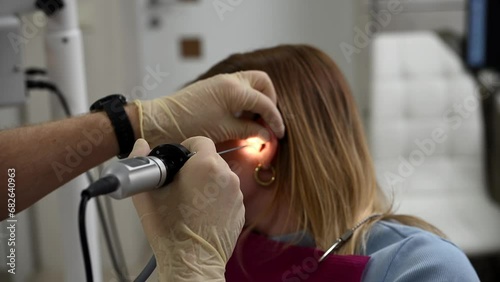 otolaryngologist conducts medical examination of ear with otoscope closeup photo