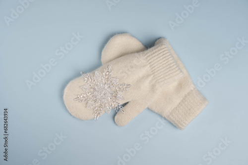 Warm white winter mittens with snowflake on blue background. Top view, flat lay.