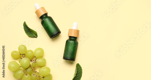 Bottles of essential oil, ripe grapes and mint leaves on beige background with space for text