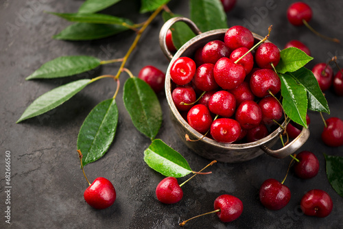Cherry summer background. A large number of cherries with leaves on the table in a saucepan on a black background. close-up.
