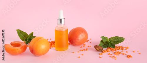 Bottle of essential oil, ripe apricots and mint leaves on pink background