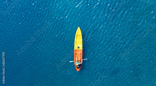 Top view of a woman paddling a yellow and orange kayak on the surface water blue sea. Woman doing water sports activities