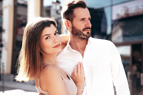 Beautiful fashion woman and her handsome elegant boyfriend in white shirt. Sexy brunette model in summer clothes. Fashionable smiling couple posing in street Europe. Brutal man and female outdoors