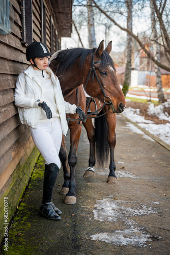 Stylish blond professional female jockey standing near horse. Friendship with horse