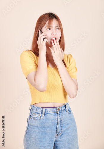 Upset stylish caucasian girl talking on phone, standing with smartphone against yellow studio background. Young Asian woman. stressed and sad. girl emotions. Using mobile phone.