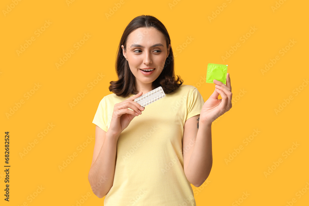 Beautiful young woman with condom and birth control pills on yellow background. Safe sex concept Beautiful young woman with condom and birth control pills on yellow background. Safe sex concept