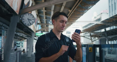 Male traveler use mobile phone in subway station while waiting for arrival upcoming subway train. Man 30s passenger in public transport stop waits for tram in city. Transportation with technology