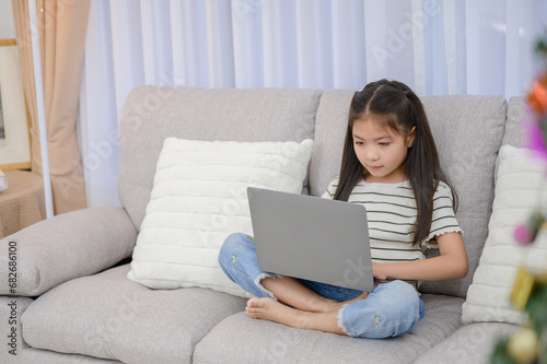 Portrait of a young Asian girl enjoying holiday activities. For education and learning that is fun and happy with using a laptop computer on the sofa in the living room at home