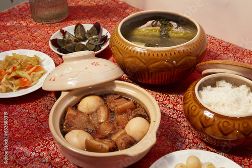 Family dinning table of Tet holiday or Lunar New Year with traditional foods: pork belly and eggs braised in coconut water, pickles, rice, Banh Tet (rice cake), fried vegetables, bitter melon soup