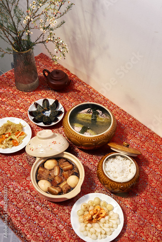 Family dinning table of Tet holiday or Lunar New Year with traditional foods: pork belly and eggs braised in coconut water, pickles, rice, Banh Tet (rice cake), fried vegetables, bitter melon soup