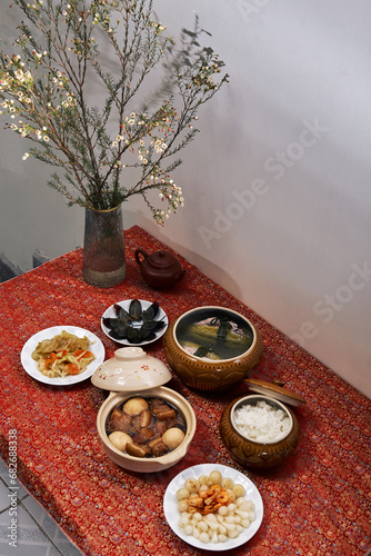 Family dinning table of Tet holiday or Lunar New Year with traditional foods: pork belly and eggs braised in coconut water, pickles, rice, Banh Tet (rice cake), fried vegetables, bitter melon soup