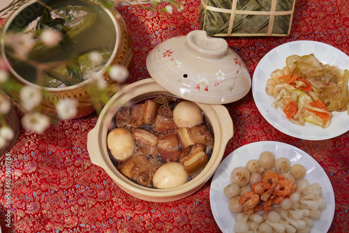 Family dinning table of Tet holiday or Lunar New Year with traditional foods: pork belly and eggs braised in coconut water, pickles, rice, Banh Tet (rice cake), fried vegetables, bitter melon soup