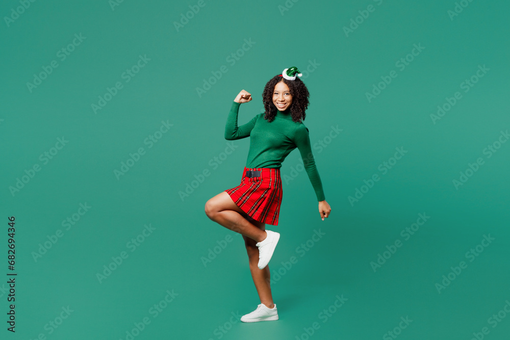Full body side view merry little kid teen girl wear hat casual clothes posing do winner gesture raise up leg isolated on plain green background. Happy New Year celebration Christmas holiday concept. Full body side view merry little kid teen girl wear hat casual clothes posing do winner gesture raise up leg isolated on plain green background. Happy New Year celebration Christmas holiday concept.