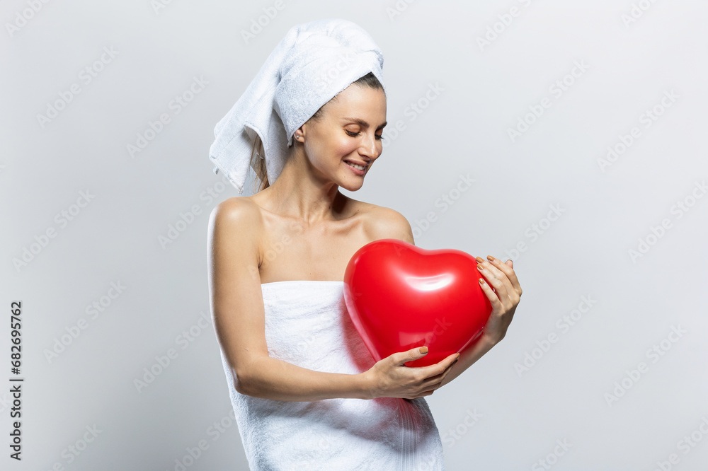 Beautiful and joyful woman wearing white towels and holding a red heart. Valentine's Day Beautiful and joyful woman wearing white towels and holding a red heart. Valentine's Day