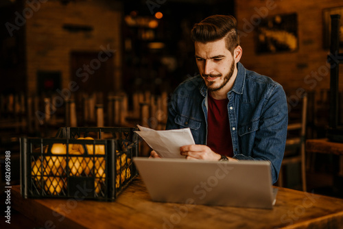 Fotografi Business-minded restaurateur counting money and updating records on a laptop