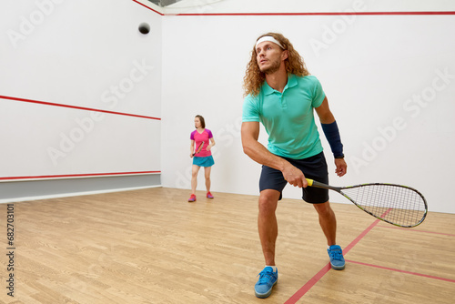 Squash male player with racket playing game with female friend