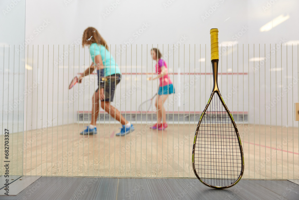 Squash game concept with racket leaned on net and sportspeople playing