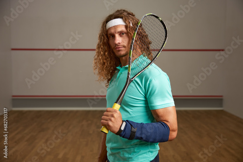 Portrait of confident male squash player standing with racket ready for game