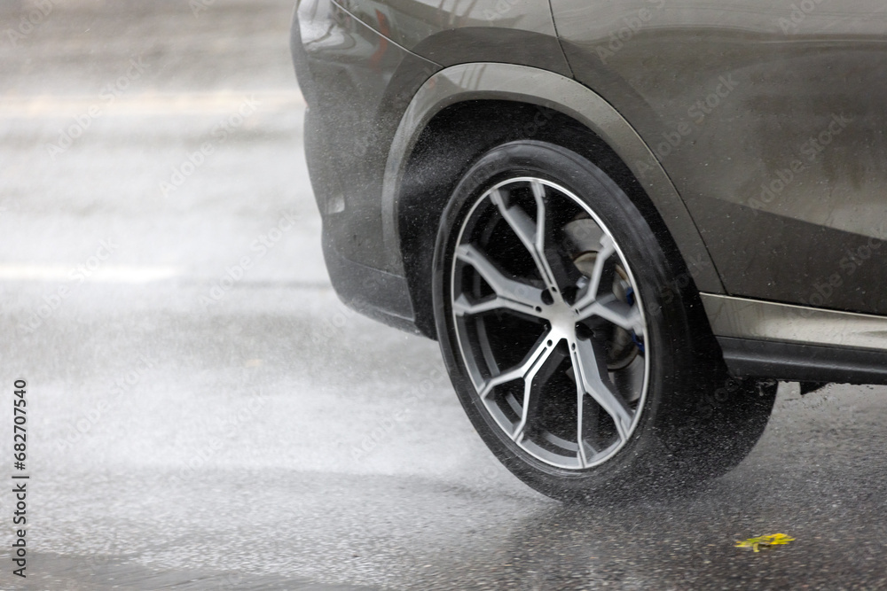 rain water splashing flows from wheels of grey car that moving fast on asphalt road