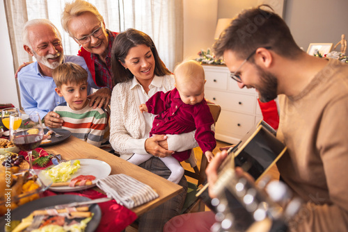 Happy multi-generation family playing the guitar and singing while having Christmas dinner