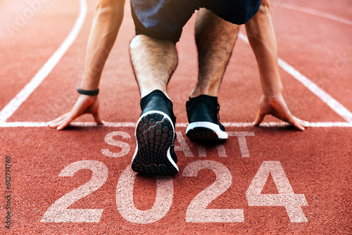 Rear view of a man preparing to start on an athletics track engraved with the year 2024.Happy New Year 2024.challenge, career path and change, readiness of leaders. Goals and plans for the next year. photo