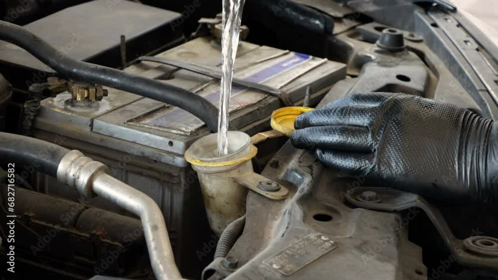 Repairman pours in to the car windscreen cleaning washer fluid liquid car glass cleaner. Water tank wiper on car engine room. Flow windshield fluid into the windshield washer reservoir Repairman pours in to the car windscreen cleaning washer fluid liquid car glass cleaner. Water tank wiper on car engine room. Flow windshield fluid into the windshield washer reservoir