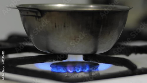 Bowl of water warmed on a dirty old gas stove at home. Water is boiling in a metal pot, close up. Poverty destitution misery concept
