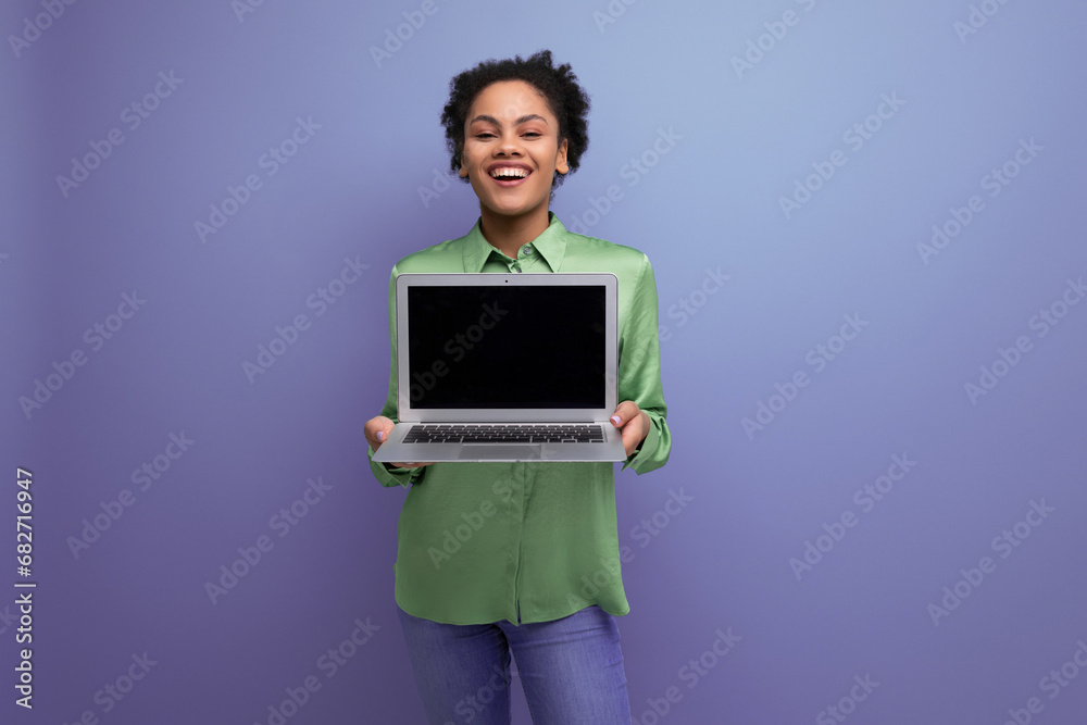 young cheerful positive hispanic brunette lady dressed in a green stylish blouse holds a laptop with a mockup on the background with copy space young cheerful positive hispanic brunette lady dressed in a green stylish blouse holds a laptop with a mockup on the background with copy space
