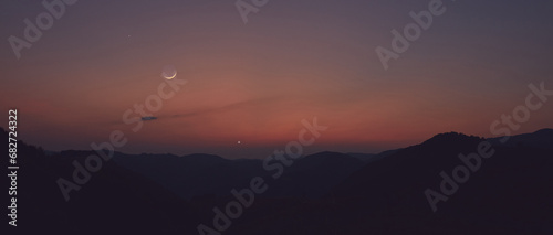 Silhouette of a mountain landscape with Milky Way stars, planets and crescent Moon.