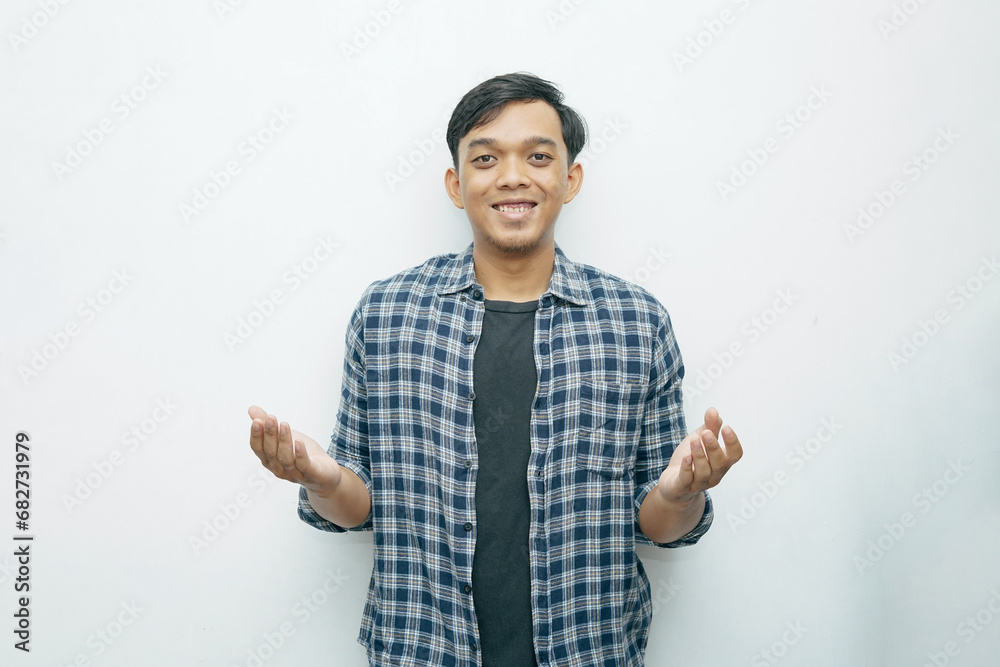 Portrait of young Indonesian Asian man smiling while put hand palms in front of his body for presenting something gesturing Portrait of young Indonesian Asian man smiling while put hand palms in front of his body for presenting something gesturing