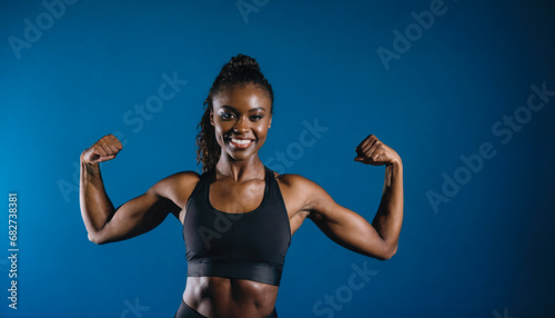 Empowering image of African American Woman Showing off Muscles in front of Blue Background. Active Lifestyle Concept.