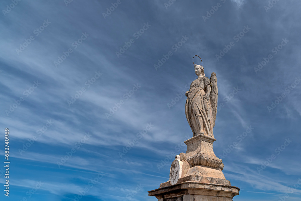 The sculpture of Saint Raphael in the middle of the Roman bridge against the cloudy sky and the ancient city of Córdoba