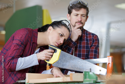 young craftswoman cutting a wooden board with a handsaw indoors photo