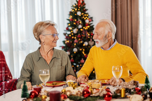 A happy senior couple is sitting at christmas table at home on christmas and new year.