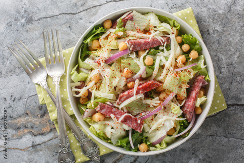 Italian American salad of salami, chickpeas, iceberg and romaine lettuce, mozzarella, onions close-up in a bowl. Horizontal top view photo