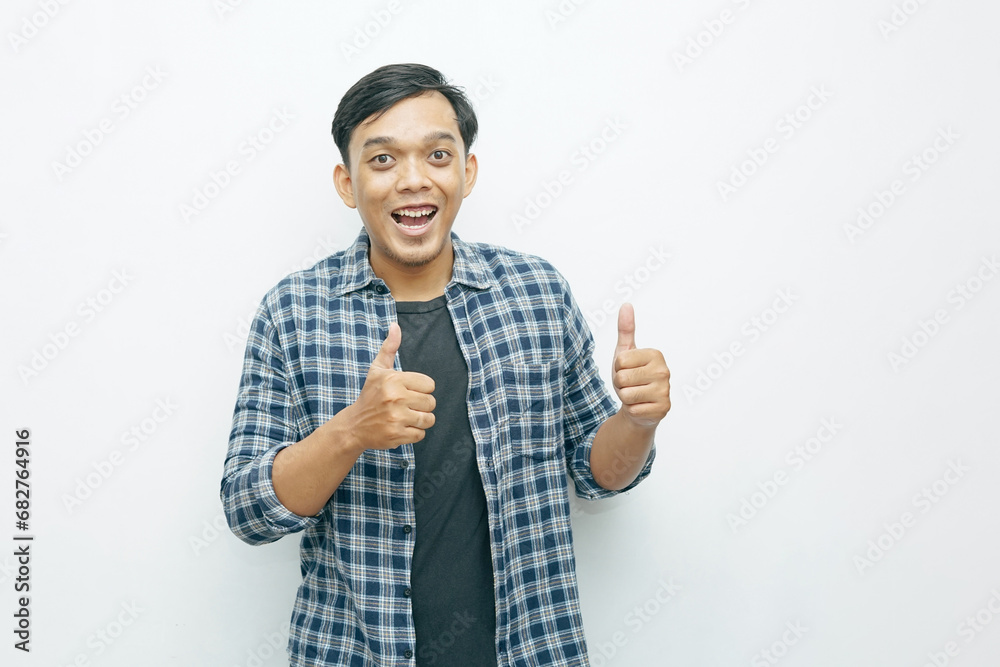 Portrait of young Asian Indonesian man smiling and showing two thumbs up as yes or successful gesture expression Portrait of young Asian Indonesian man smiling and showing two thumbs up as yes or successful gesture expression