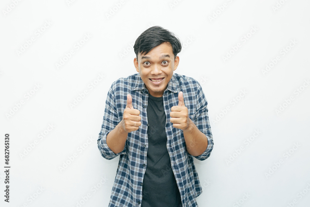Portrait of young Asian Indonesian man smiling and showing two thumbs up as yes or successful gesture expression Portrait of young Asian Indonesian man smiling and showing two thumbs up as yes or successful gesture expression