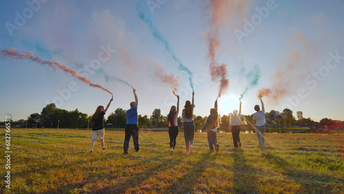 A group of friends spraying multi-colored smoke at sunset.