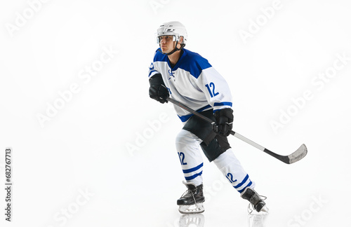 Dynamic image of young man, hockey player in motion, standing with stick, training against white studio background