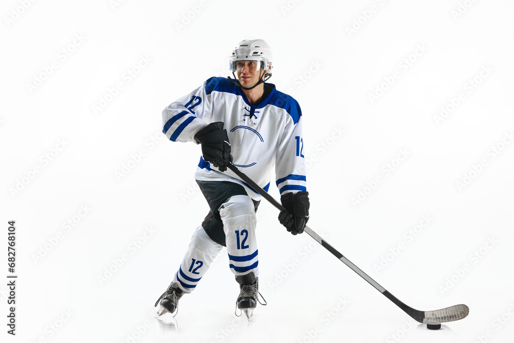 Obraz premium Young man, hockey athlete in motion, standing on rink with stick, training, playing against white studio background