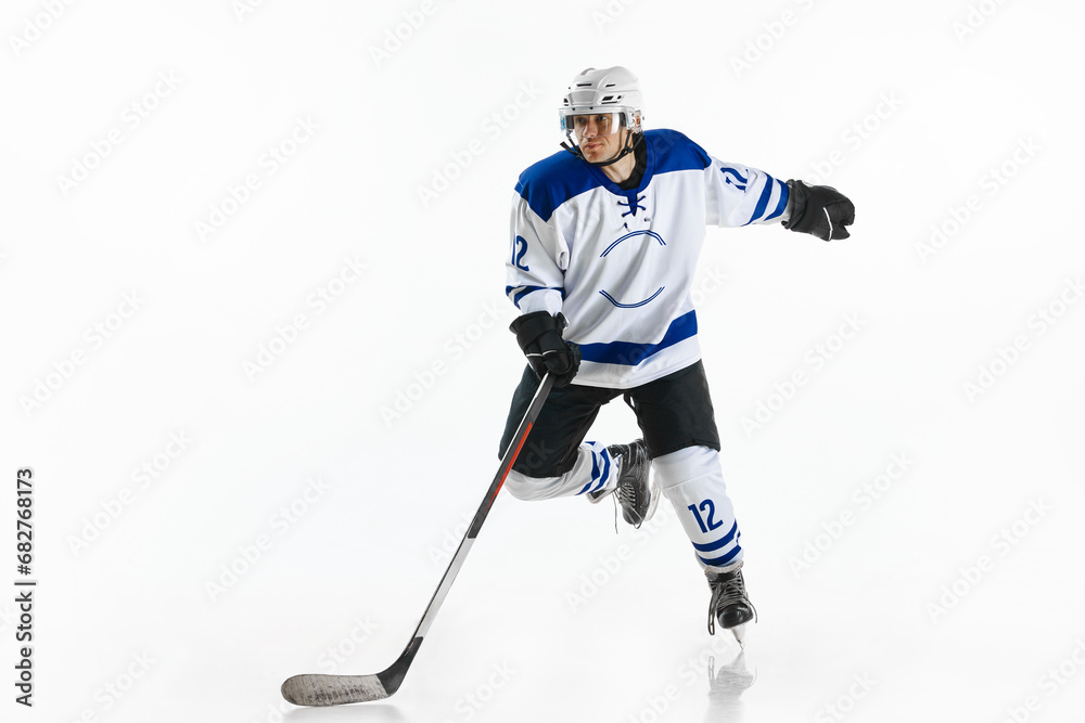Obraz premium Dynamic image of young man, hockey player in motion on rink, training, playing against white studio background
