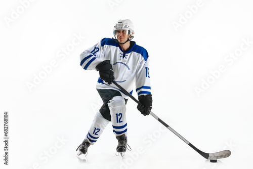 Young man, hockey athlete in motion, standing on rink with stick, training, playing against white studio background