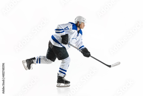 Young man, motivated athlete, hockey player in motion with stick on rink, training against white studio background