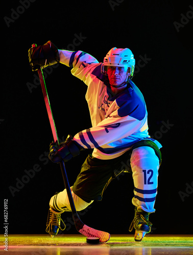 Canvas Print Concentrated young man, hockey player in uniform standing with stick and puck ag